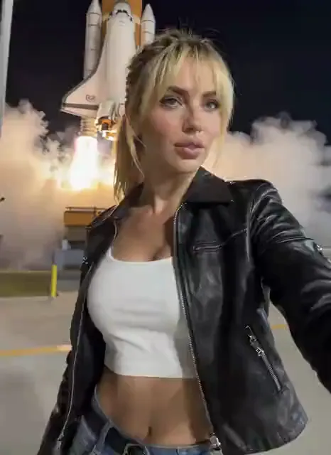 Video preview: Launch-day portrait — An adult woman records her excited reaction while a spacecraft lifts off behind her, cinematic launch atmosphere and natural handheld motion.