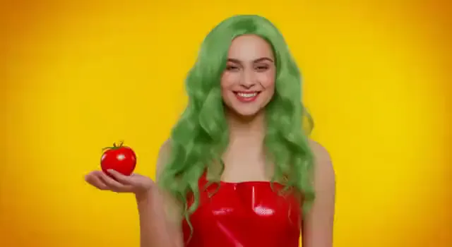 Video preview: Color pop portrait — An adult woman with green hair poses against a yellow backdrop in a red outfit, playful fashion portrait motion.